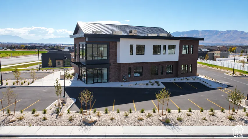 Modern two-story structure featuring a combination of brick and smooth-panel siding, a metal roof, expansive floor-to-ceiling glass windows, and a dedicated asphalt parking lot