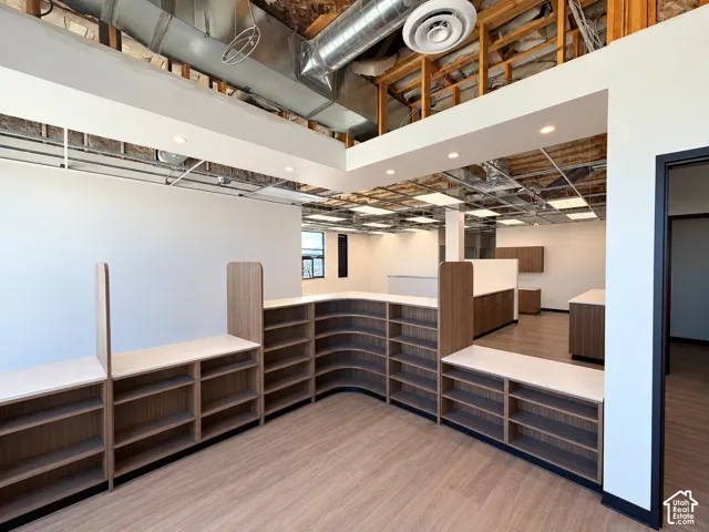 L-shaped wood-finish built-in cabinetry with integrated shelving and light-colored countertops, wood-finish flooring, and exposed ceiling infrastructure with recessed lighting