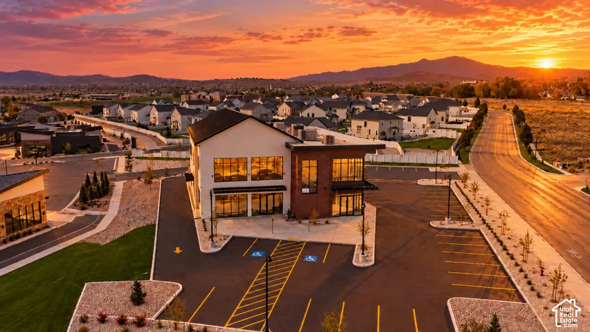 Two-story mixed-use building featuring a brick and stucco exterior, floor-to-ceiling glass windows, and a dedicated asphalt parking lot with mountain backdrop