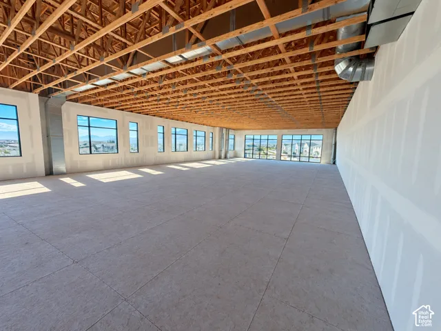 Expansive open-concept interior featuring exposed timber truss ceiling, grid-style window groupings, and unfinished wall surfaces