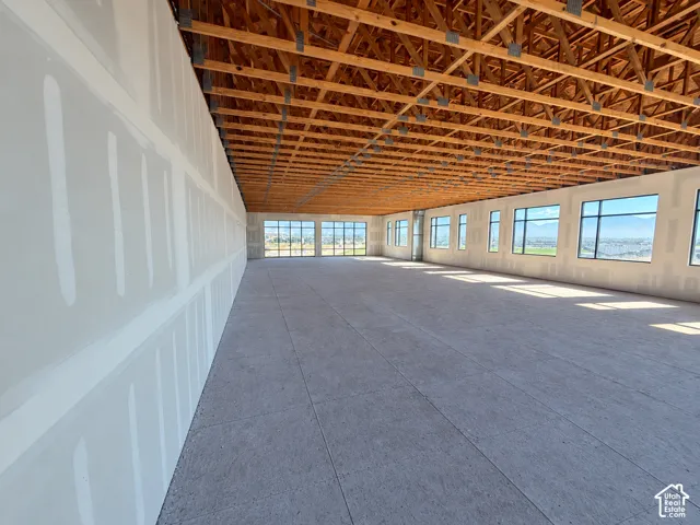 Open-concept interior featuring exposed wood-truss vaulted ceilings, concrete flooring, and multiple large windows with mountain and landscape scenery