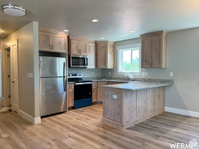Kitchen with a peninsula, stainless steel appliances, light wood-style floors, and baseboards