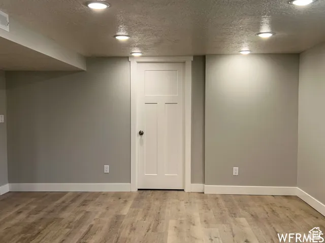 Finished below grade area with baseboards, light wood-style floors, and a textured ceiling
