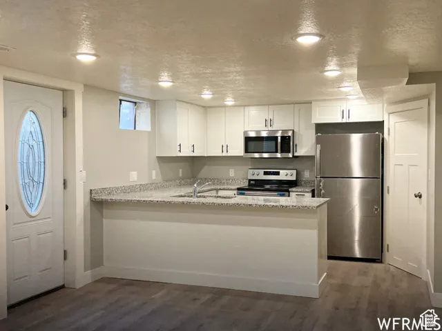 Kitchen with stainless steel appliances, a textured ceiling, a sink, white cabinets, and wood finished floors