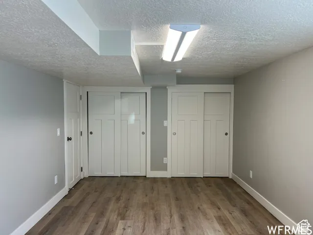 Unfurnished bedroom featuring baseboards, a textured ceiling, wood finished floors, and two closets