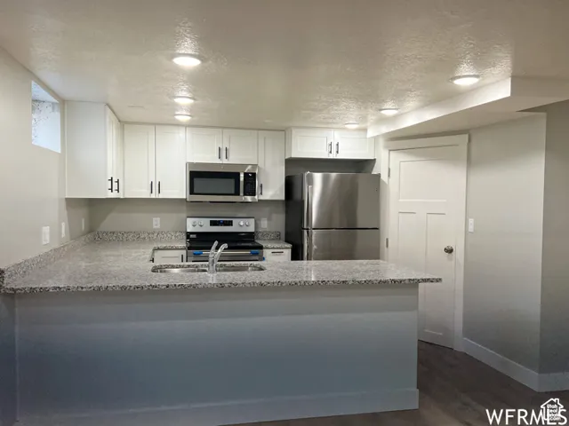 Kitchen featuring a textured ceiling, white cabinets, a peninsula, light stone countertops, and appliances with stainless steel finishes