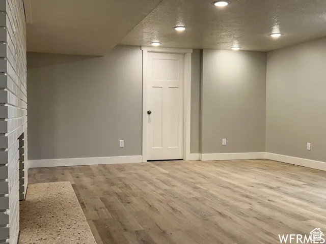 Finished below grade area featuring a textured ceiling, baseboards, and light wood-type flooring