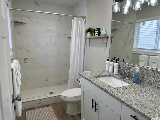 Bathroom with toilet, a tile shower, wood finished floors, and vanity