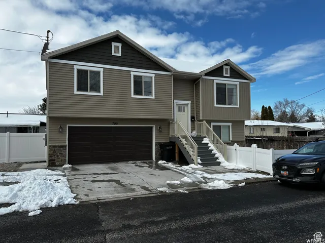 Raised ranch featuring driveway, an attached garage, fence, and stone siding