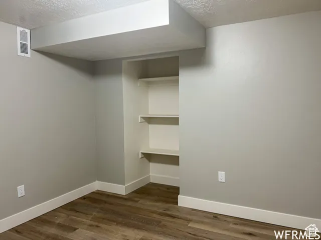 Finished basement featuring dark wood-style floors, baseboards, a textured ceiling, and visible vents