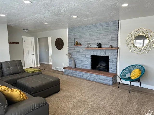 Living room with a stone fireplace, a textured ceiling, baseboards, and visible vents