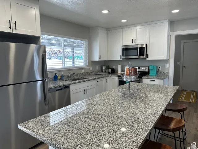 Kitchen featuring a textured ceiling, white cabinets, stainless steel appliances, a sink, and dark wood-style floors