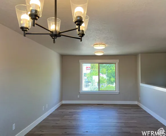 Spare room featuring dark wood-type flooring, a textured ceiling, baseboards, and a notable chandelier