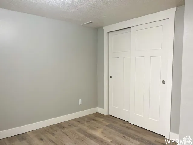 Unfurnished bedroom featuring baseboards, a closet, wood finished floors, and a textured ceiling