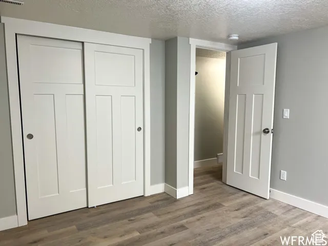 Unfurnished bedroom with baseboards, a closet, wood finished floors, and a textured ceiling