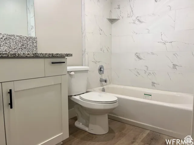 Bathroom with toilet, wood finished floors, bathtub / shower combination, and vanity