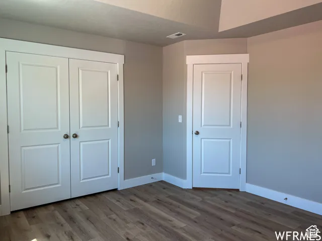 Unfurnished bedroom featuring wood finished floors, a closet, baseboards, and visible vents