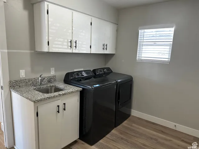 Laundry room with baseboards, washing machine and clothes dryer, a sink, cabinet space, and wood finished floors