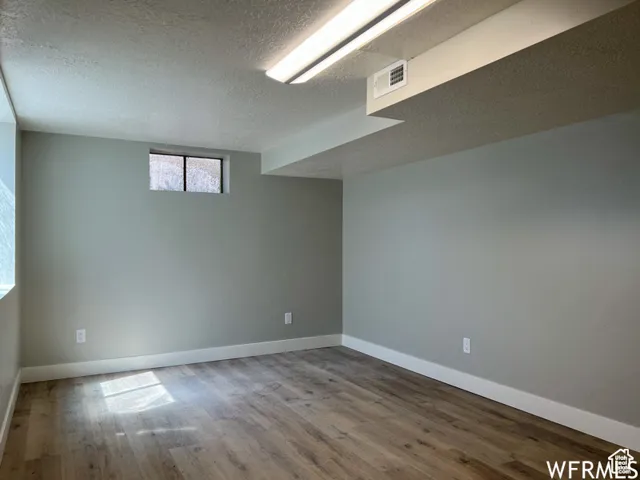 Below grade area featuring baseboards, visible vents, a textured ceiling, and wood finished floors