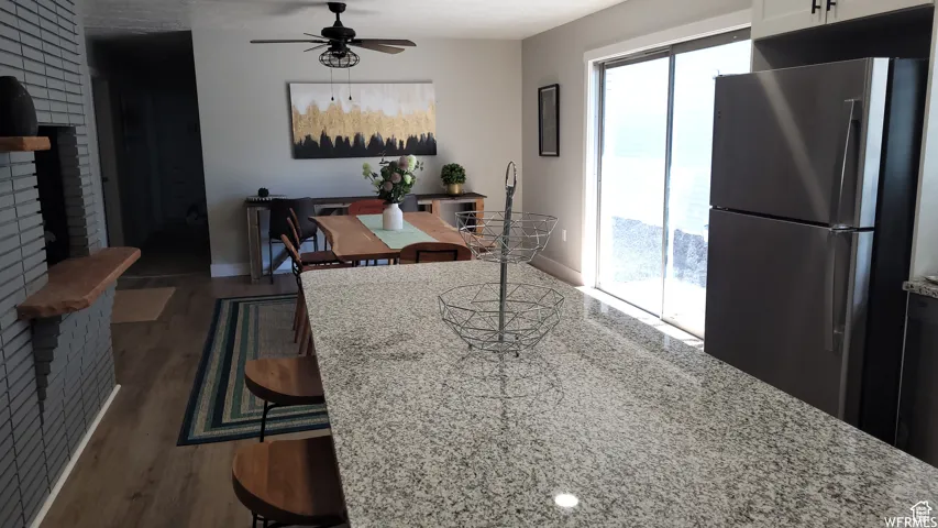 Kitchen with light stone counters, freestanding refrigerator, a ceiling fan, a fireplace, and wood finished floors