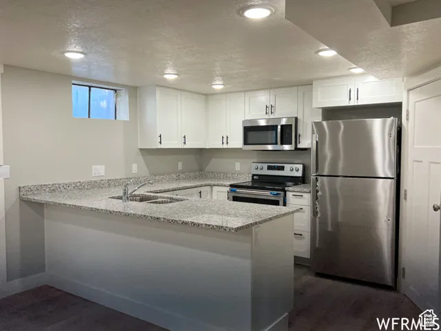 Kitchen featuring white cabinetry, a sink, stainless steel appliances, and a peninsula