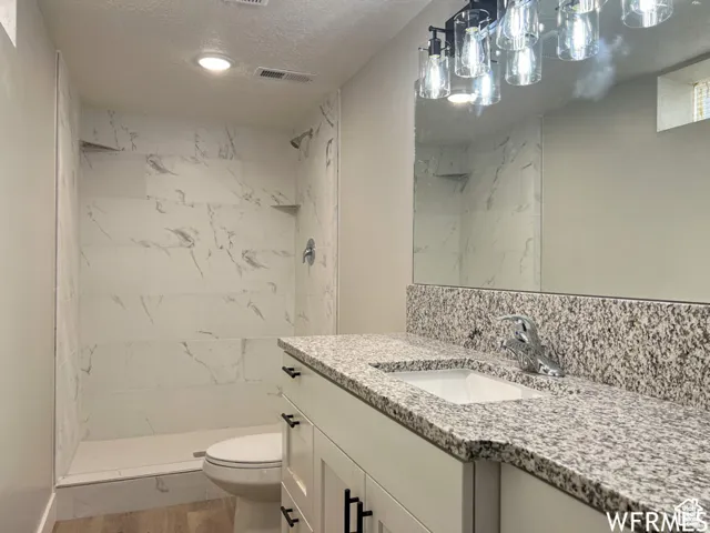 Bathroom featuring visible vents, a tile shower, toilet, and vanity
