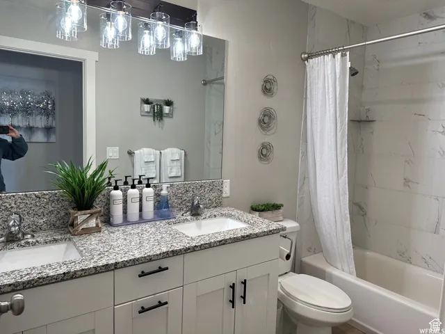 Bathroom with double vanity, toilet, shower / tub combo with curtain, and a sink