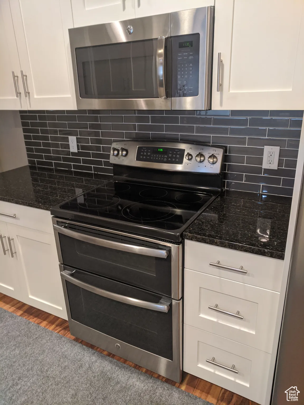Kitchen featuring decorative backsplash, white cabinets, stainless steel appliances, and dark stone counters.