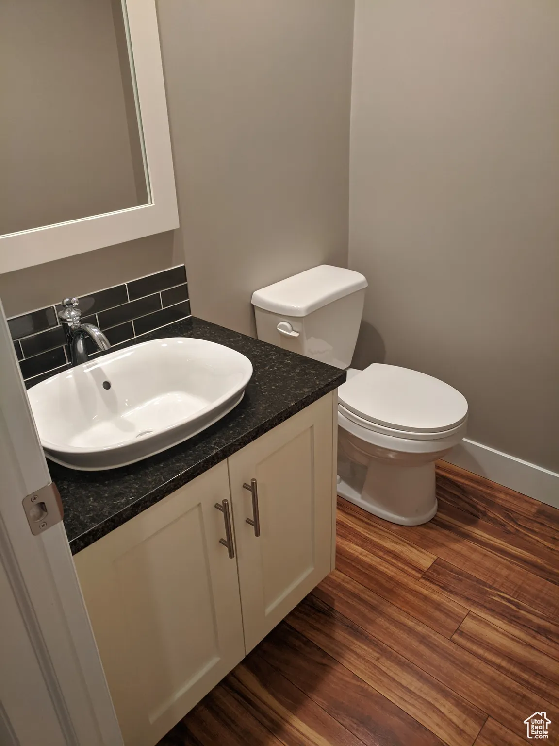 Bathroom featuring toilet, vanity, decorative backsplash, and wood finished floors