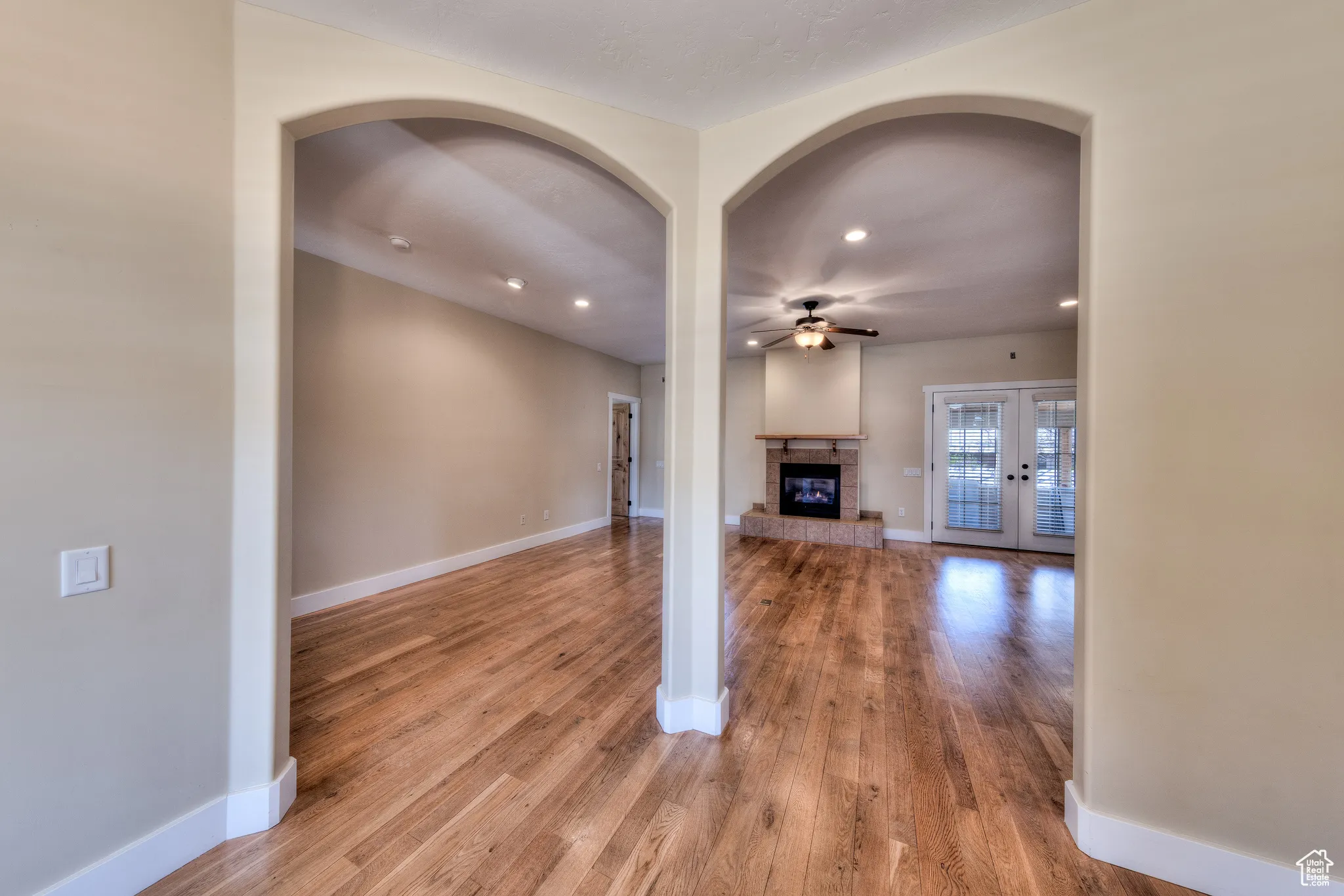 Unfurnished living room featuring baseboards, wood finished floors, a glass covered fireplace, and a ceiling fan