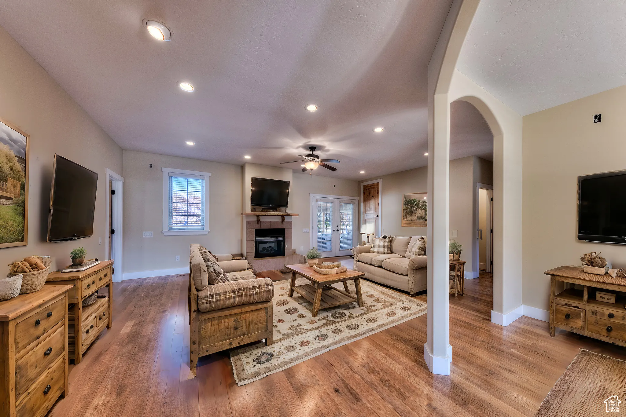 Living area featuring arched walkways, a tile fireplace, light wood-style floors, and a ceiling fan