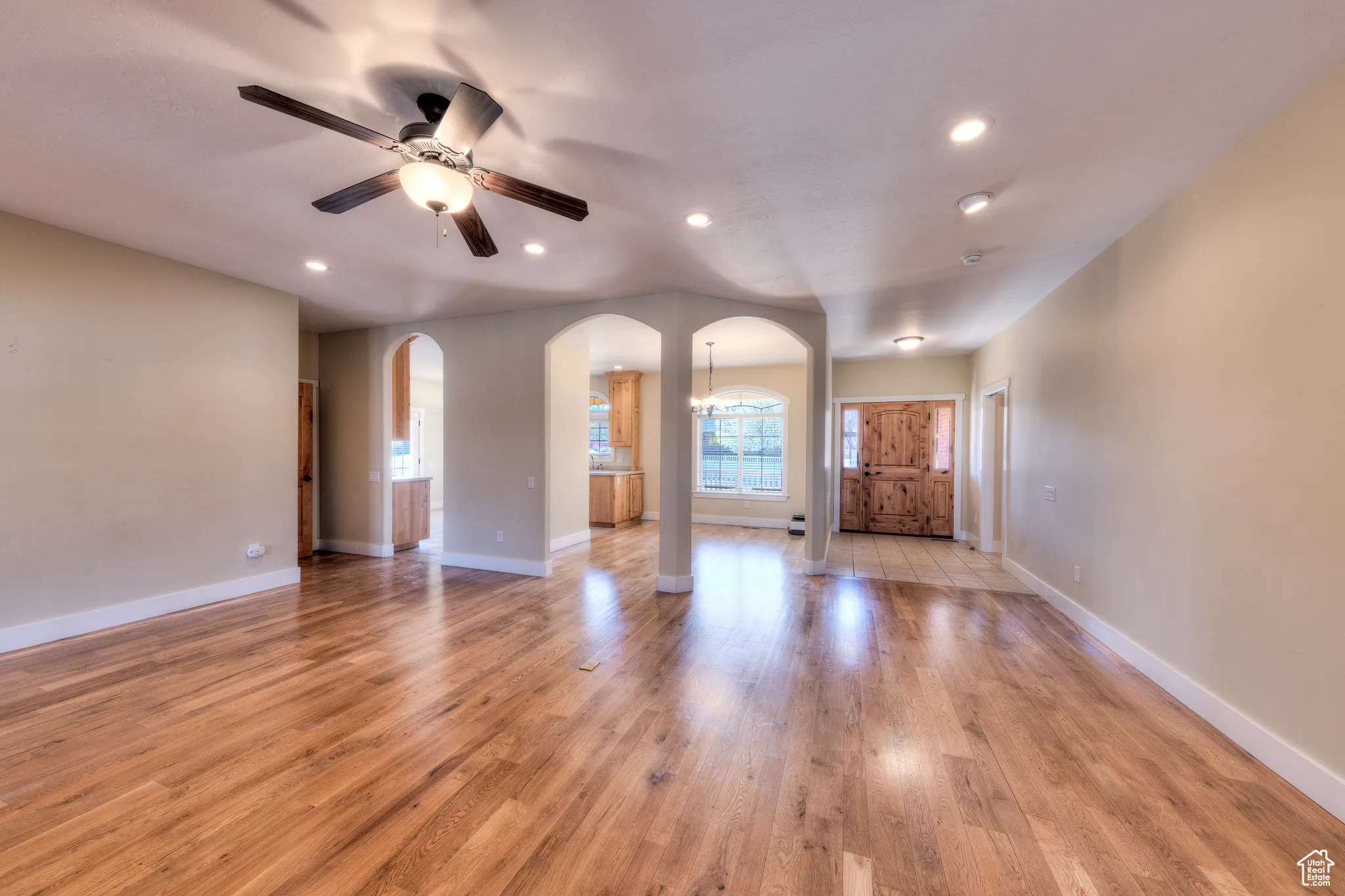 Unfurnished living room featuring light wood-style flooring, baseboards, arched walkways, and a ceiling fan