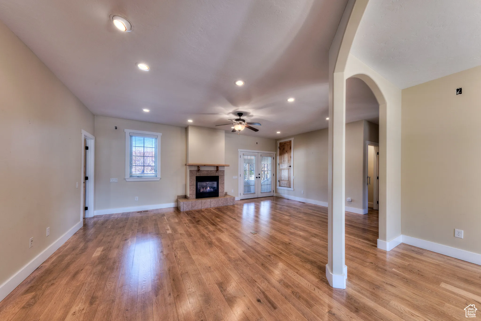 Unfurnished living room with baseboards, a tiled fireplace, light wood-style flooring, and a ceiling fan