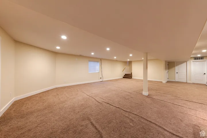 Finished basement featuring light carpet, baseboards, stairway, and recessed lighting