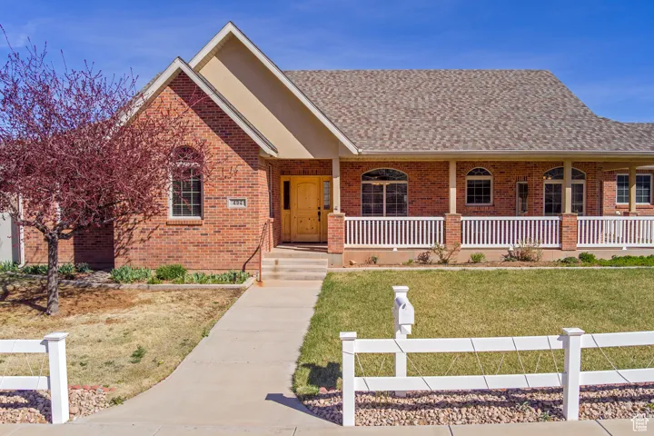 View of front facade featuring covered porch, a shingled roof, a front lawn, and brick siding