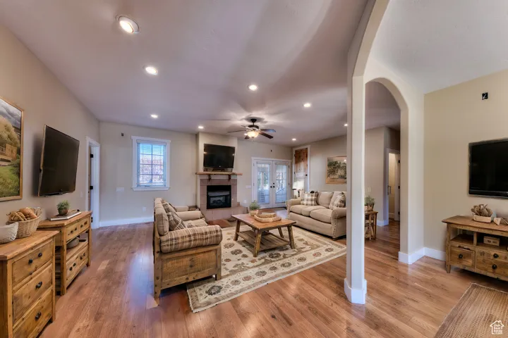 Living area featuring arched walkways, a tile fireplace, light wood-style floors, and a ceiling fan