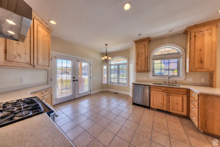 Kitchen with light countertops, a sink, a chandelier, wall chimney exhaust hood, and stainless steel dishwasher