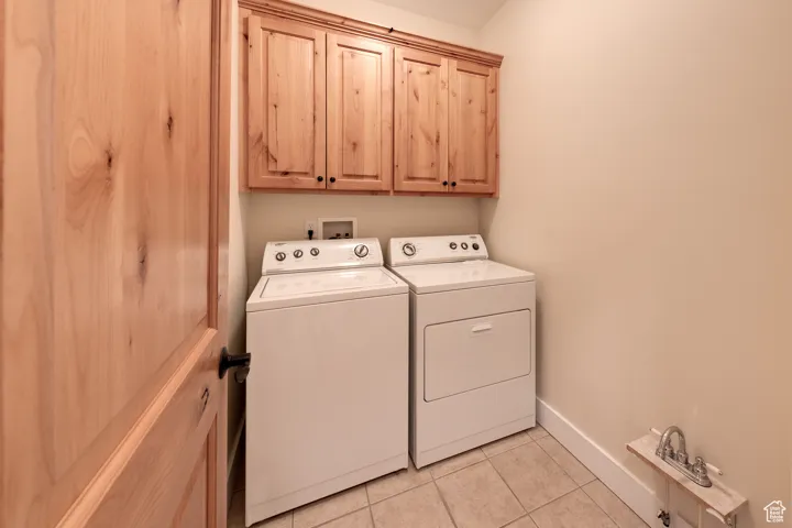 Laundry room with light tile patterned floors, cabinet space, baseboards, and washer and dryer