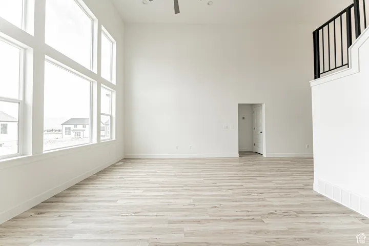 Spare room with ceiling fan, plenty of natural light, a high ceiling, and light wood-style flooring