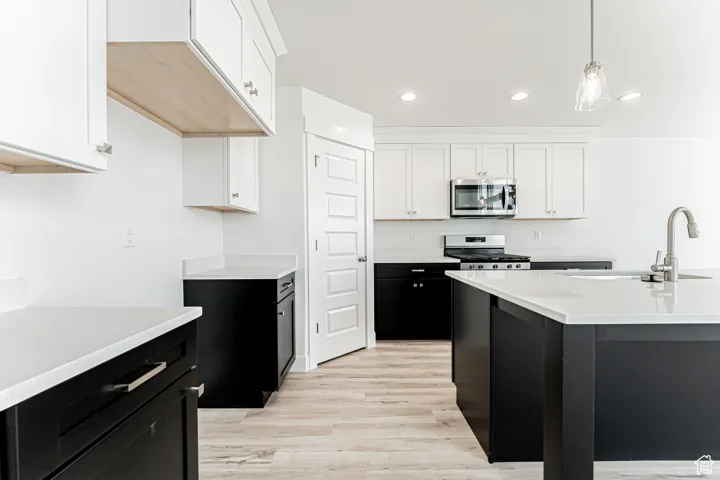 Kitchen featuring stainless steel microwave, range, dark cabinetry, light countertops, and white cabinets