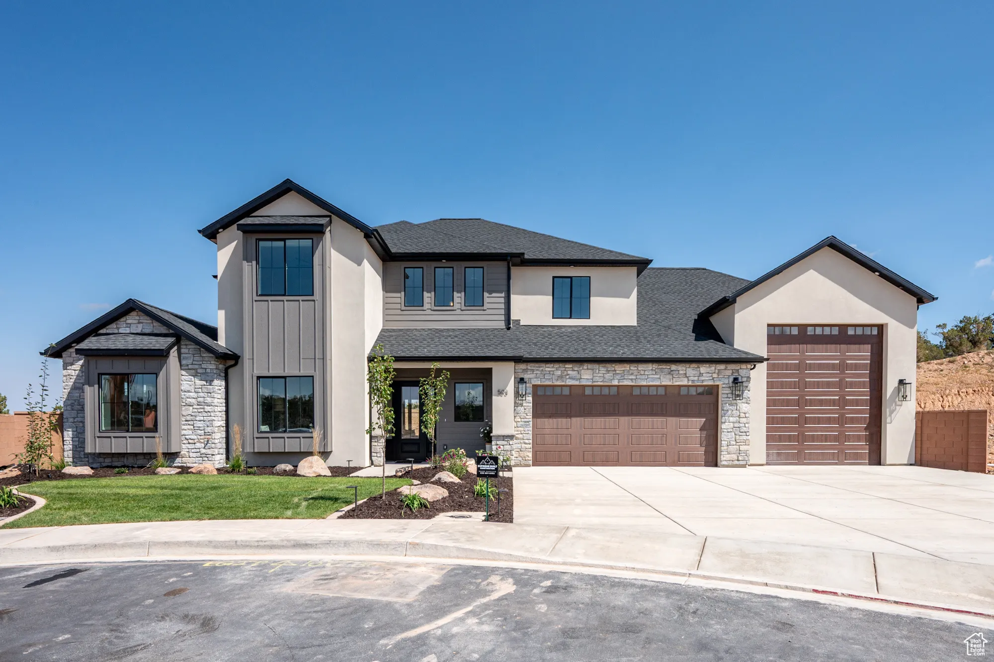 View of front facade with stone siding, driveway, an attached garage, roof with shingles, and a front yard