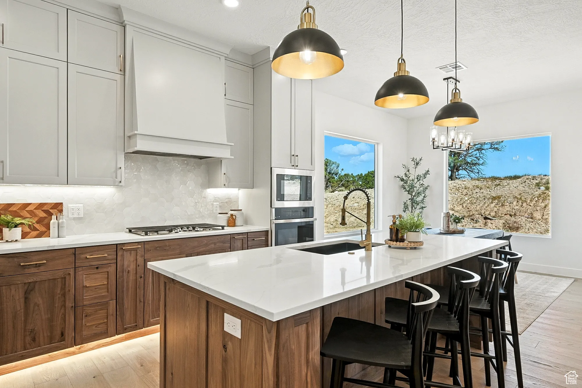 Kitchen featuring decorative backsplash, hanging light fixtures, light wood-type flooring, light stone countertops, and a textured ceiling