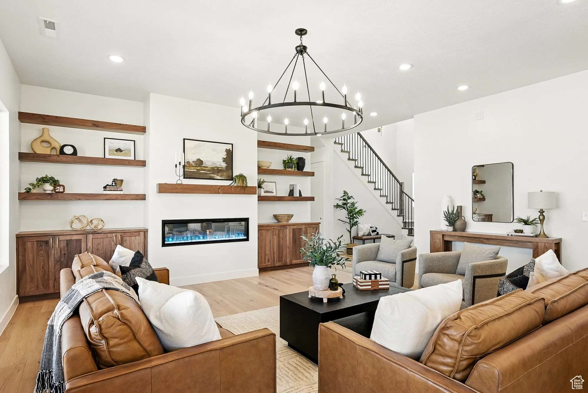 Living area featuring a glass covered fireplace, built in shelves, light wood-style flooring, recessed lighting, and stairs