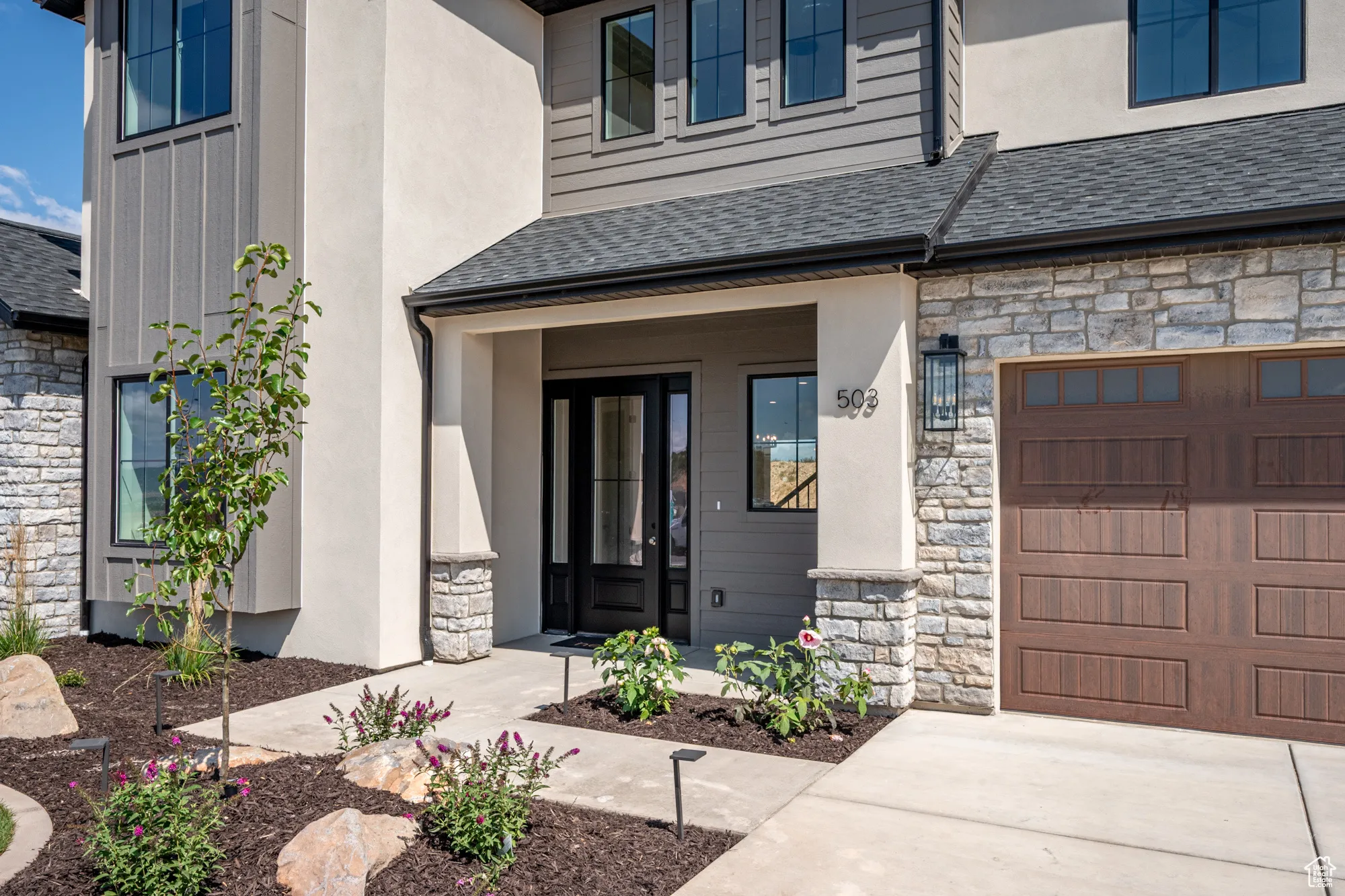 Doorway to property featuring stone siding, a shingled roof, stucco siding, and a garage