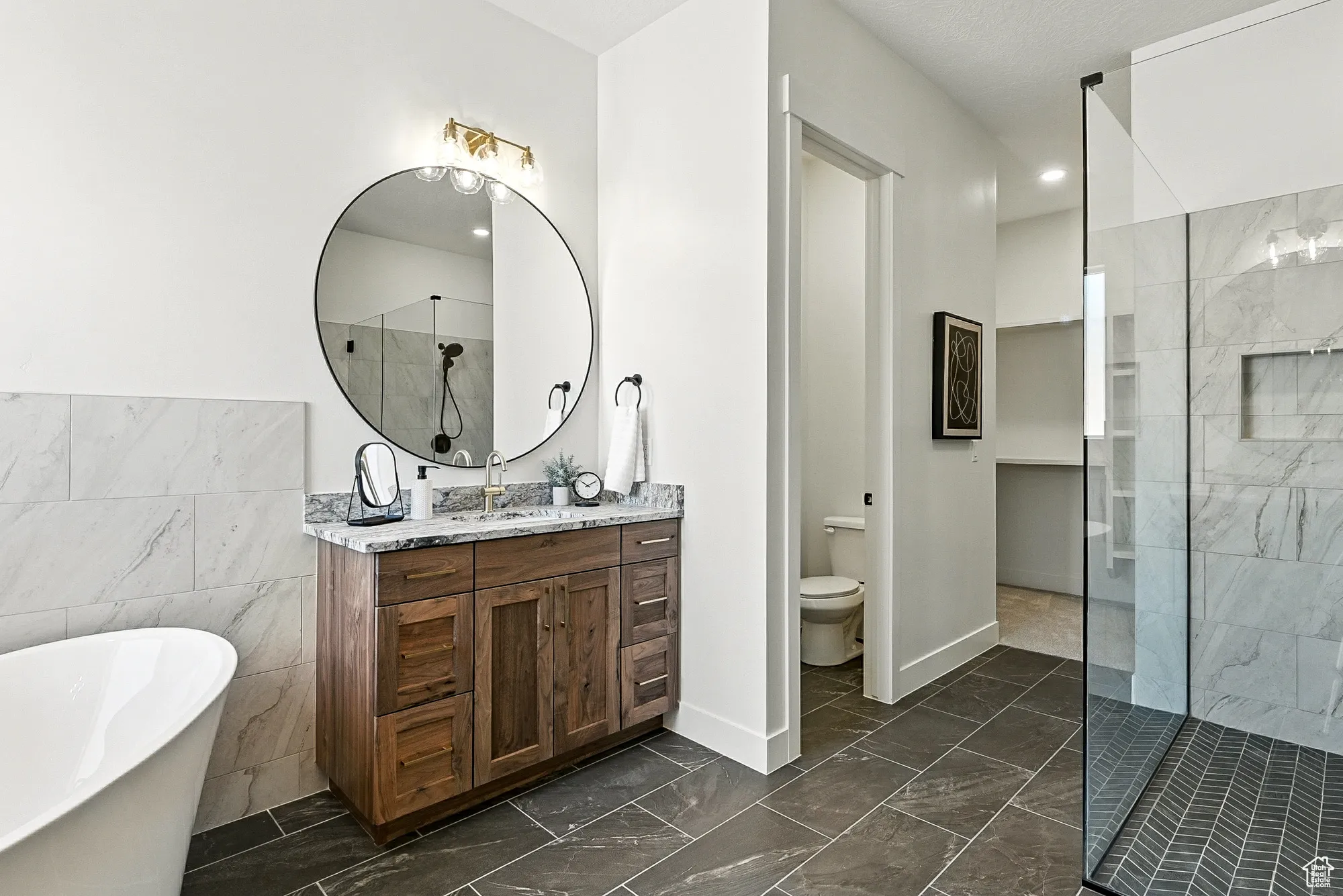 Bathroom with walk in shower, vanity, a freestanding tub, tile walls, and dark marble finish floors