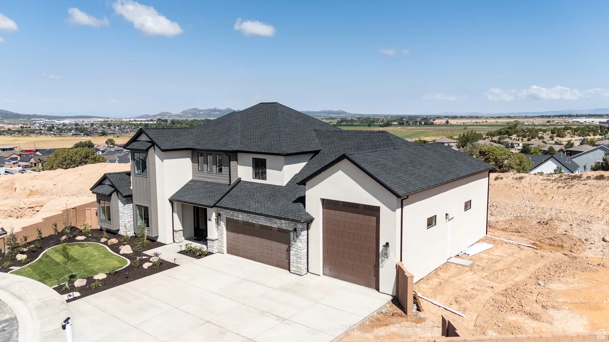 View of front of property featuring roof with shingles, stone siding, concrete driveway, an attached garage, and a mountain view