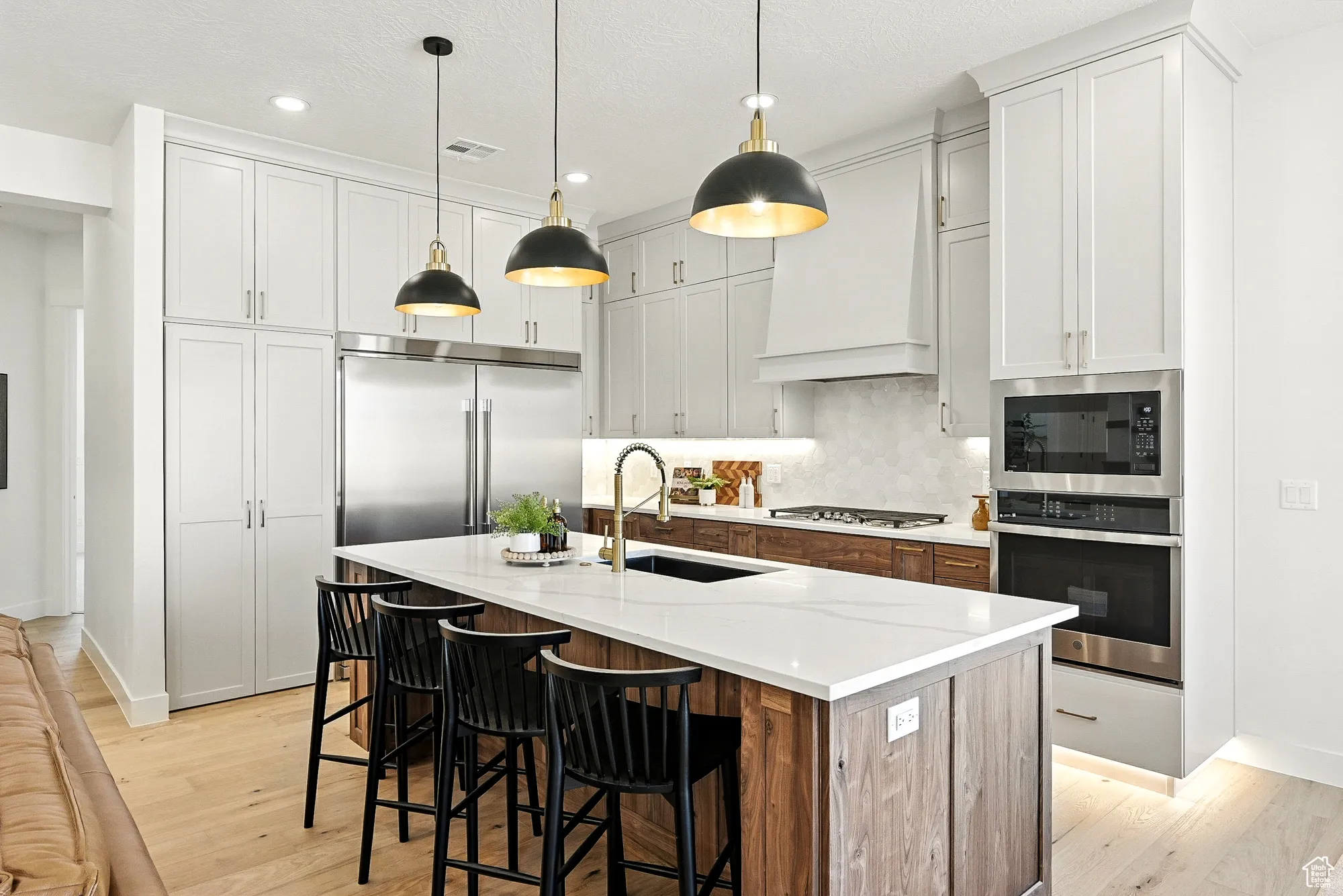 Kitchen with tasteful backsplash, built in appliances, an island with sink, a breakfast bar area, and hanging light fixtures