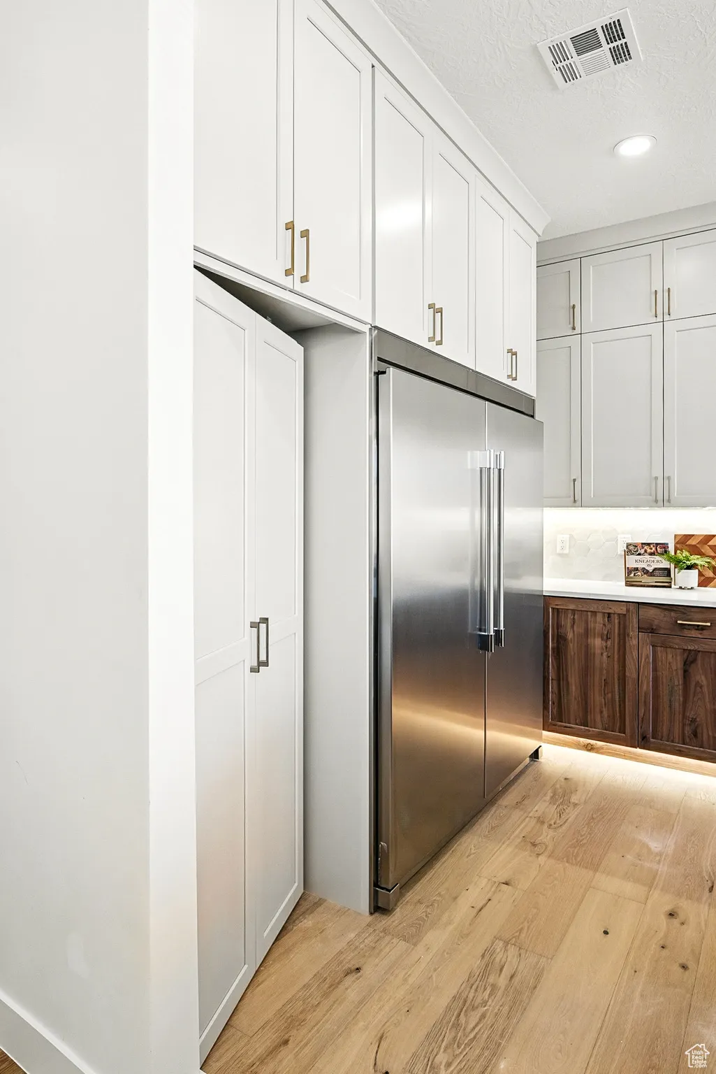 Kitchen with light wood finished floors, stainless steel built in refrigerator, white cabinetry, a textured ceiling, and recessed lighting