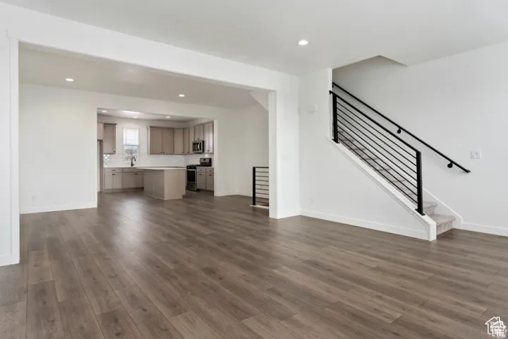 Unfurnished living room featuring dark wood-style floors, baseboards, stairs, and recessed lighting