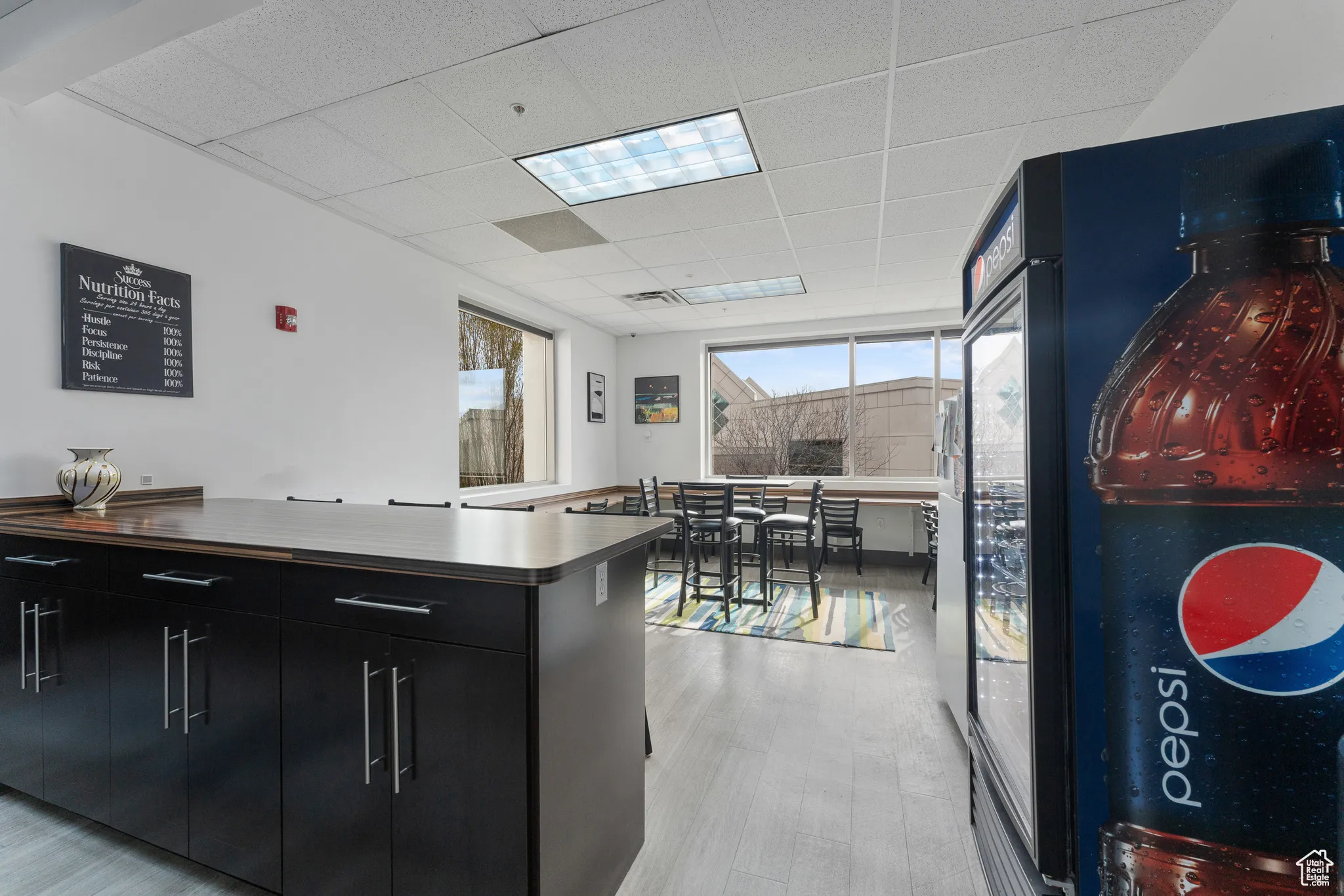 Kitchen with black refrigerator, light wood-style flooring, a drop ceiling, and dark cabinetry